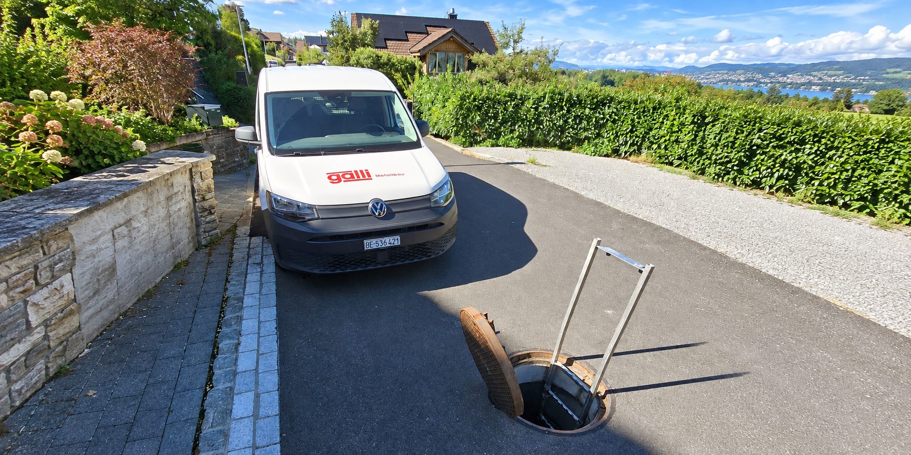 Geöffneter Strassenschacht mit eingebauter Schachtleiter und Servicefahrzeug der Galli Metallbau AG